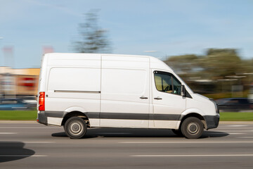 A white van drives fast down the street. Commercial vehicles for small loads, parcel deliveries. Motion blur