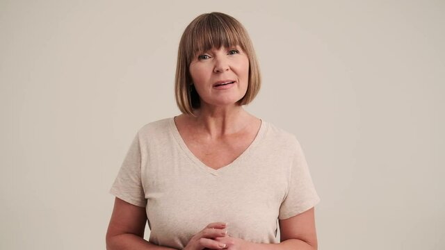 A positive cheerful mature woman with bob hairstyle listen the viewer and disagree with something at the camera on gray-beige background in studio