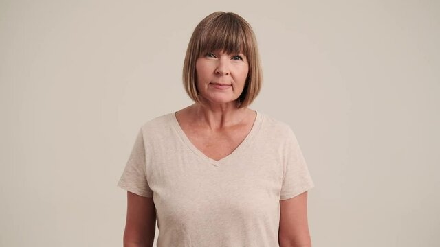 An offended angry mature woman with bob hairstyle peering at the camera on gray-beige background in studio