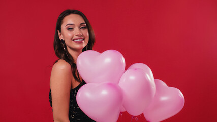 happy woman in black dress holding pink balloons isolated on red.