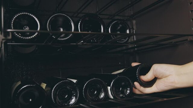 Close up 4K of red wine bottles stored in wine cellar with cooling to preserve in a row of racks for drinking and seeing people hand which is put the wine bottle in shelf as collection at house.