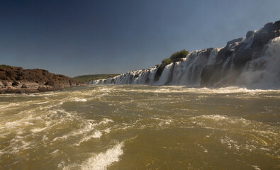 Navigating the rapids. The majestic Mocona falls seen from the boat. The rocky waterfall white water, strong river current flowing across the jungle.