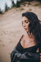 Naklejka premium sexy brunette in makeup and jewelry posing on the sand in black lingerie