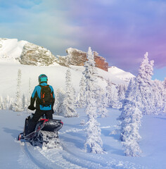 a snowmobiler travels through a snow-covered forest in the mountains against the background of beautiful rocks. the perfect photo for advertising snowmobile tourism. snowbike. snow motorcycle