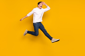 Fototapeta na wymiar Full length profile photo of impressed brunet young guy jump look wear shirt jeans sneakers isolated on yellow background