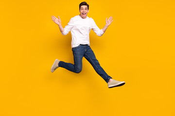 Full size photo of funny brunet millennial guy jump wear shirt jeans sneakers isolated on yellow background
