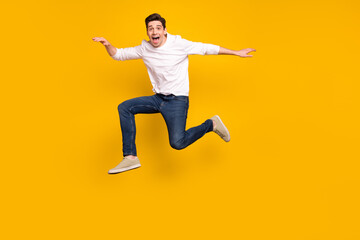 Full body photo of cool brunet young guy jump wear shirt jeans sneakers isolated on yellow background