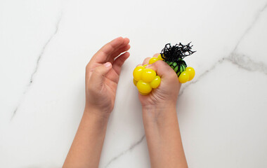 The child does an exercise with a relief ball for tactile sensations. Easy sensory classes for kids. Small hands hold a yellow stress ball on a white background. Selective focus.