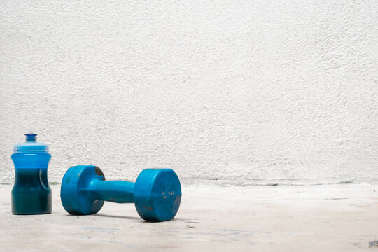 blue dumbbell and bottle with water on the floor (used, dusty and abandoned) white background, exercise at home, space for text. exercise and health concept. fitness concept