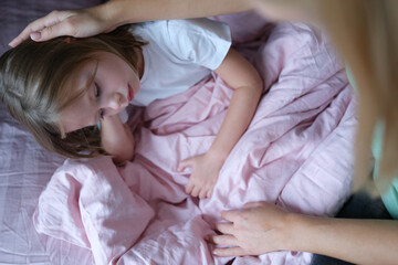 Mother stroking head of little sad girl lying in bed
