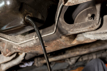 Old and dirty oil is drained from the underchassis of an SUV. Maintenance procedure of a diesel...