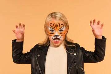 angry girl with tiger face painting growling and showing scary gesture isolated on beige