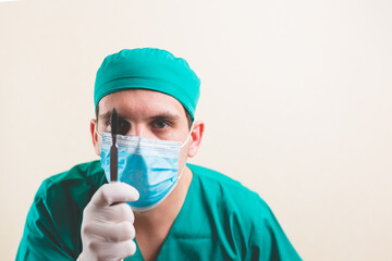 Focused doctor in green surgeon suit and protective breathing mask with lancet on the yellow background isolated