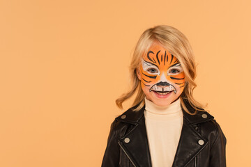 happy child in tiger makeup smiling at camera isolated on beige