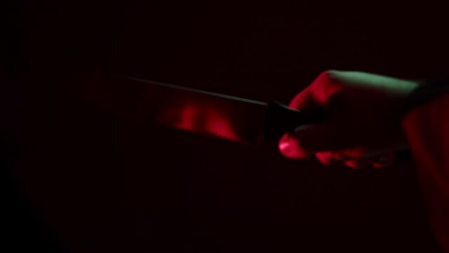 Reflection of evil killer in knife close-up. Psycho murderer hand holding sharp weapon for killing victims. Halloween time. Concept of horror film or nightmare. 