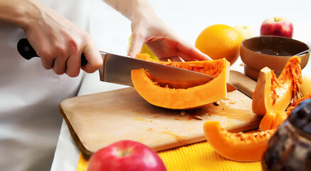 Closeup female hands are cutting a pumpkin with a knife.