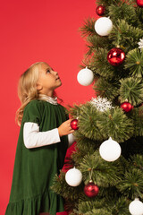 girl in green dress looking at decorated christmas tree isolated on red