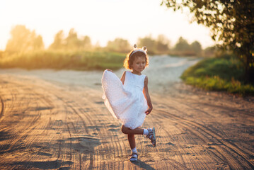 Little girl in a white dress outdoors at sunset time.