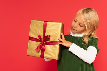 girl in green dress looking at present in golden wrapping paper on red