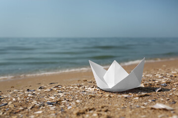 Fototapeta na wymiar White paper boat on sandy beach near sea, space for text
