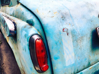 Old rusted abandoned blue retro car, red taillight, peeling paint on the automobile up close....