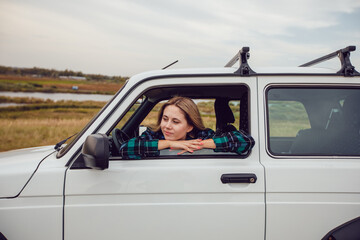 A young woman looks out of the window of an SUV and admires the nature.