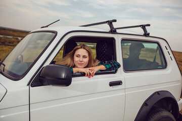 A young woman looks out of the window of an SUV and admires the nature.