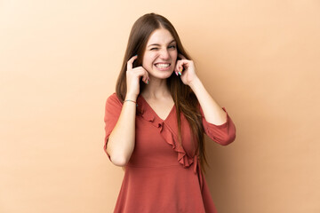 Young caucasian woman isolated on beige background frustrated and covering ears