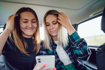 Two women use the phone while sitting in the car.