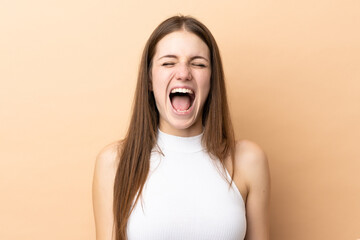 Young caucasian woman isolated on beige background shouting to the front with mouth wide open