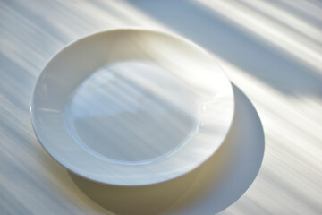 White plate saucer on a white background with sun shadows