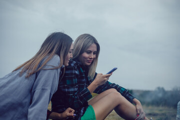 Obraz premium Couple of girls sitting in nature cute chatting using smartphone.