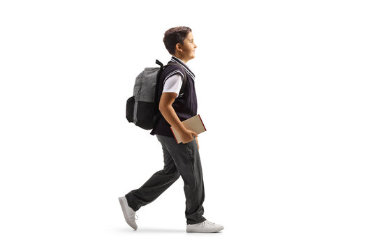 Full length profile shot of a schoolboy in a uniform walking with a book in his hand