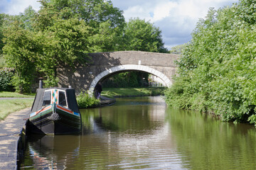 Fototapeta na wymiar A quiet stretch of the Leeds and Liverpool Canal near Barnoldswick, with a single narrowboat moored alongside the tow-path, and an old canal bridge in the middle distance.