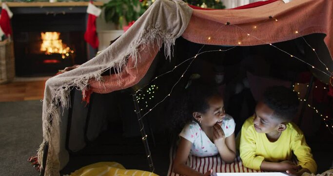 Happy african american siblings using tablet in makeshift tent