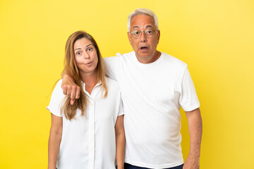 Middle age couple isolated on yellow background with surprise facial expression