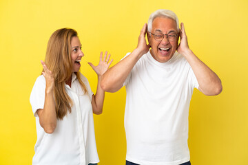 Middle age couple isolated on yellow background frustrated and shouting