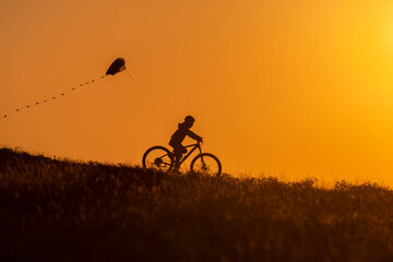 Obraz premium Silhouette of a child riding a bicycle with a kite in his hand