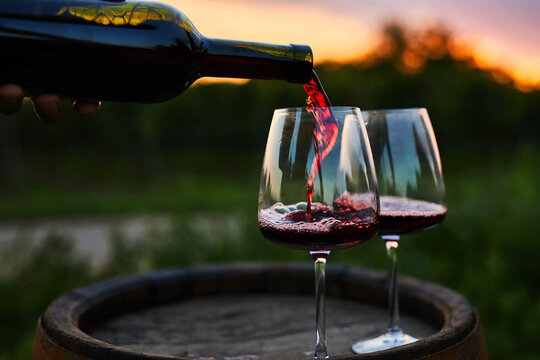 Pouring red wine into glasses on the barrel at dusk