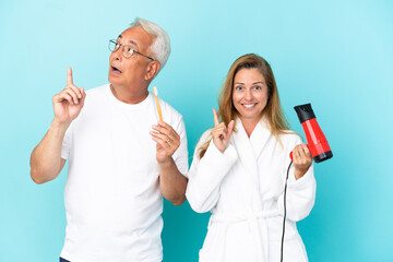 Middle age couple holding dryer and toothbrush isolated on blue background thinking an idea pointing the finger up