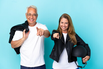 Middle age bikers couple with a motorcycle helmet isolated on blue background points finger at you with a confident expression