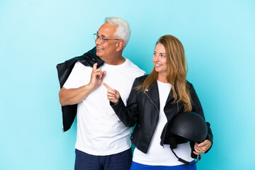 Middle age bikers couple with a motorcycle helmet isolated on blue background presenting an idea while looking smiling towards