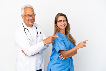 Middle age doctor and nurse isolated on white background pointing finger to the side in lateral...