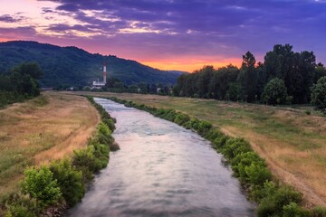Panoramic view of blurred motion Nisava river in Pirot and distant old factory during vivid, colorful sunset