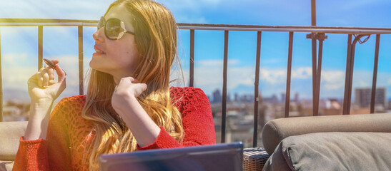 Happy young woman enjoying city view from rooftop on a sunny day using laptop