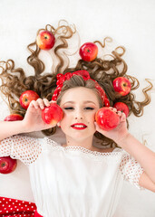 girl in lies in red apples and holds apples