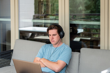 Young man using headphones with laptop computer on outdoor couch