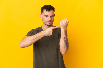 Young caucasian handsome man isolated on yellow background making the gesture of being late