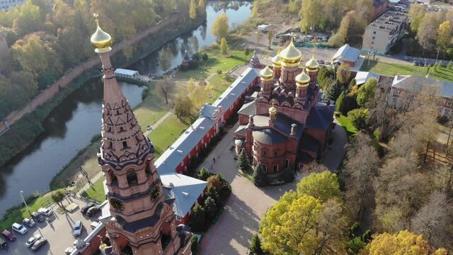 Aerial drone view of bell tower and red-brick cathedral on the background of the river at sunny autumn day. Gethsemane Chernigov Skete, Sergiyev Posad, Russia in 4K