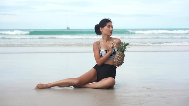happy girl holding a pinapple cocktail on a beach. Tourism and recreation in Thailand. Charming cute Asian woman travel around the islands. The girl enjoy life and has fun. Paradise beaches and white